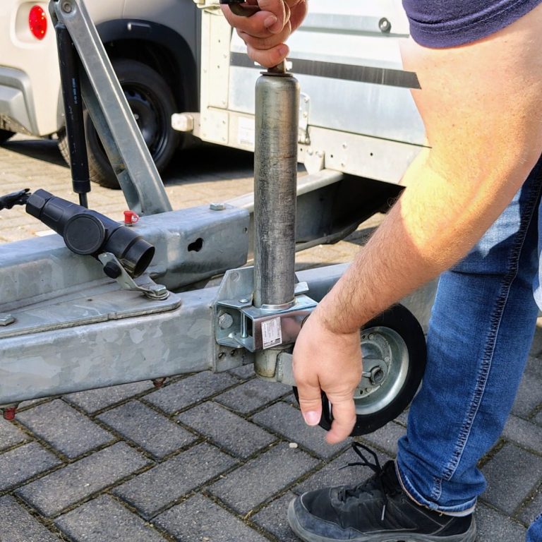 Eine Person sichert einen Anhänger mit einer Handkurbel an einem Gestell.