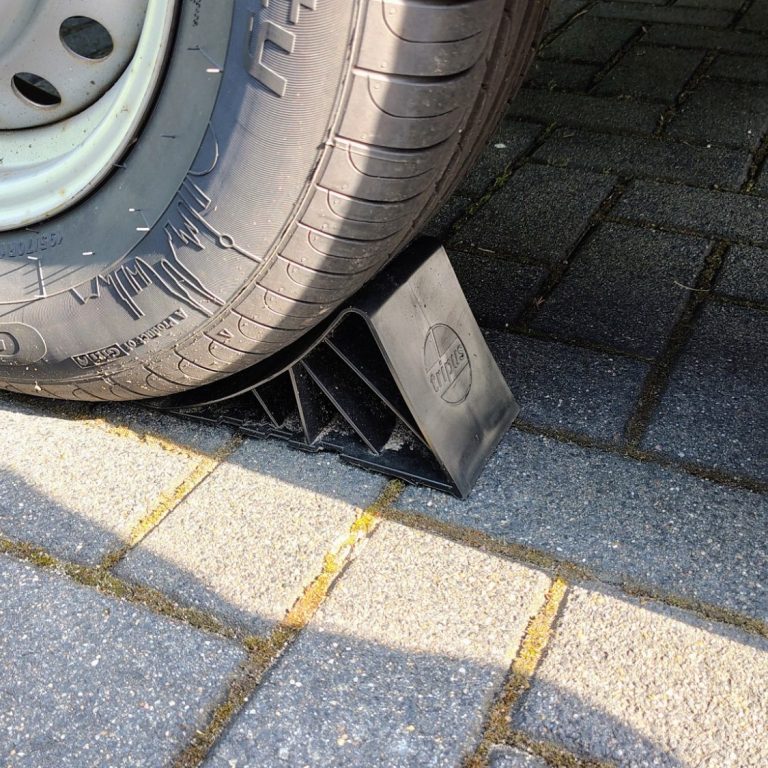 Ein schwarzer Keil unter einem Reifen auf gepflastertem Untergrund.